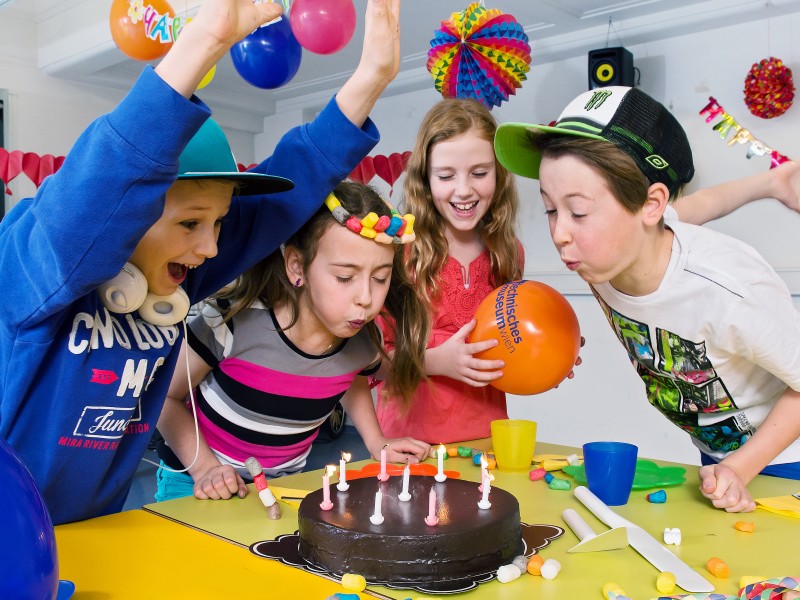 Children are celebrating a birthday party in the partyroom with a lot of decoration and a cake: 